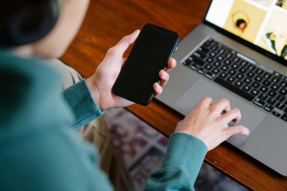 A person works on a laptop while checking a smartphone, capturing the constant switching between tools.